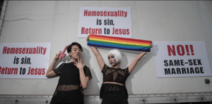 Photo of two people, one holding a pink toy gun, the other holding a rainbow banner